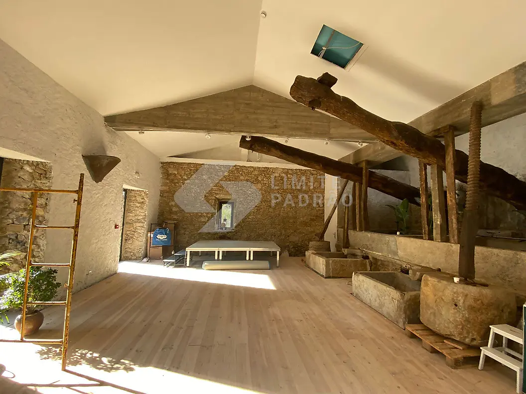 Reabilitação de interior: salão rústico com paredes em pedra, asnas e lagar antigo