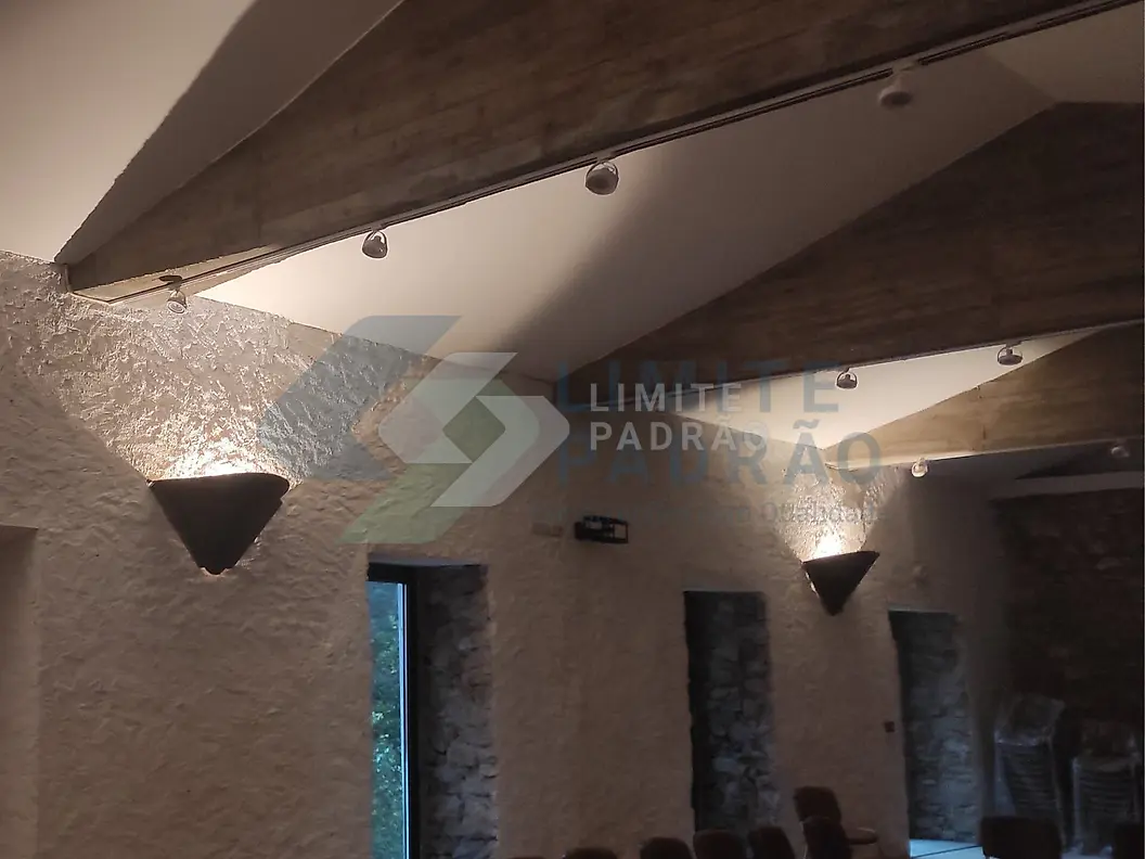 Reabilitação de interior: salão rústico com asnas, paredes em pedra e apliques