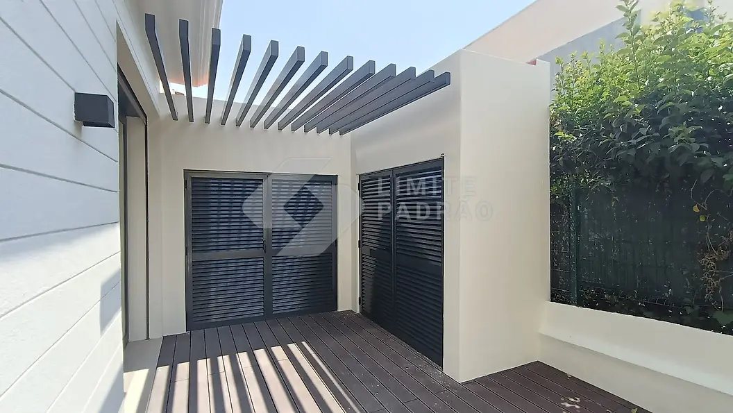 Pátio com pérgola e deck: pérgola de lâminas em alumínio e pavimento em deck compósito, junto à moradia