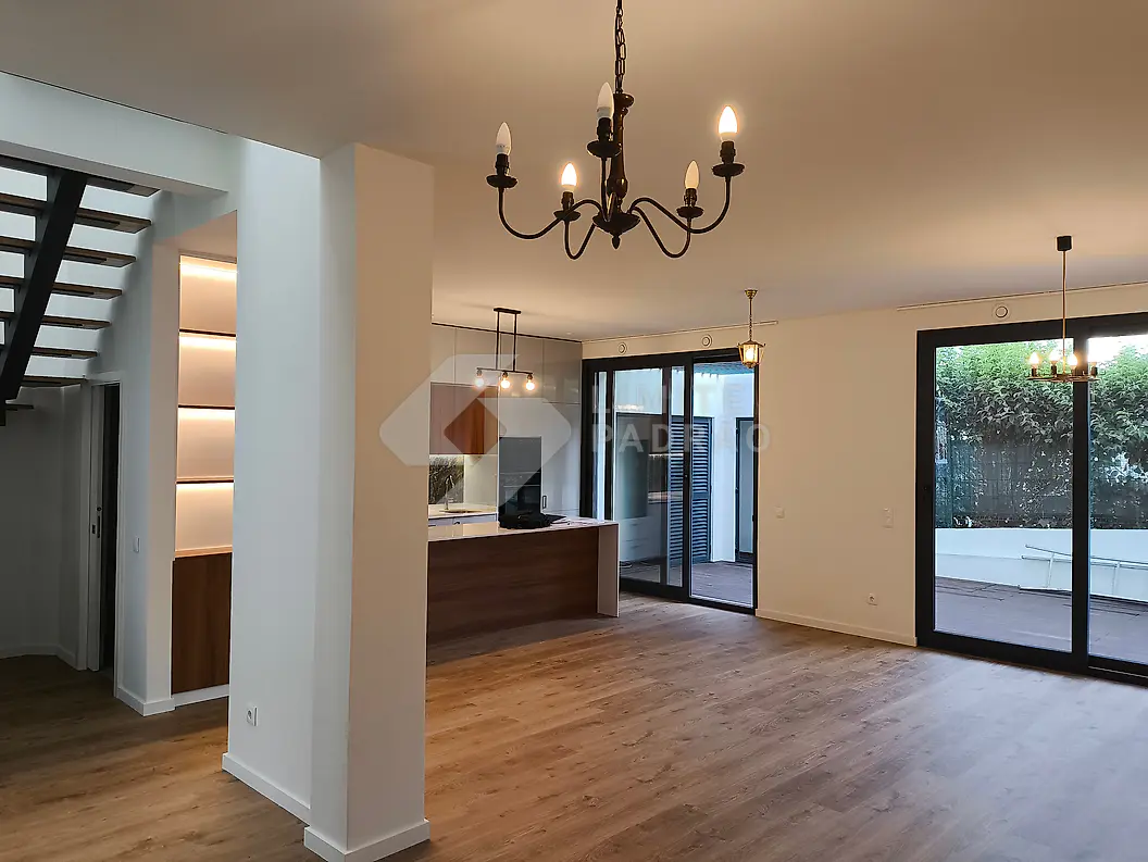 Sala em open space: sala e cozinha num só espaço, lustres e grandes vãos envidraçados para o pátio