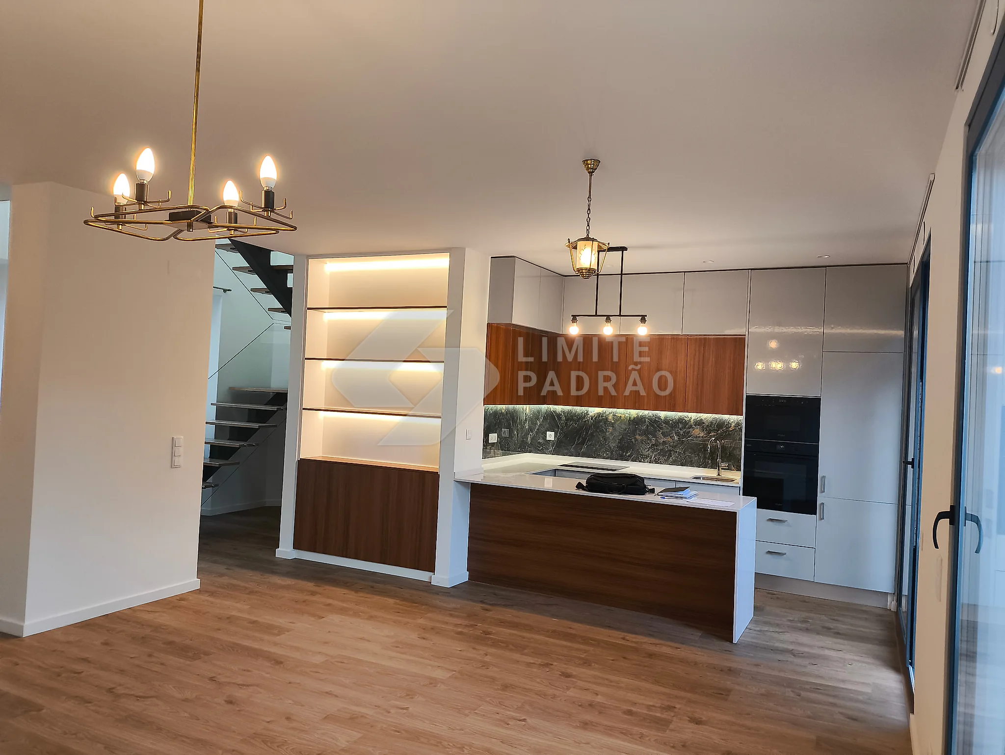 Cozinha com ilha: ilha central, estante iluminada por LED, lustre e escada ao fundo