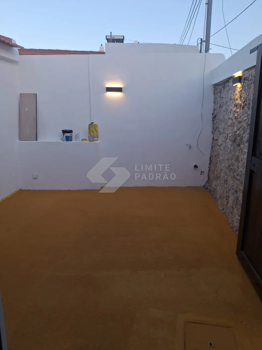 Pátio: muros pintados de branco, parede em pedra e aplique de luz