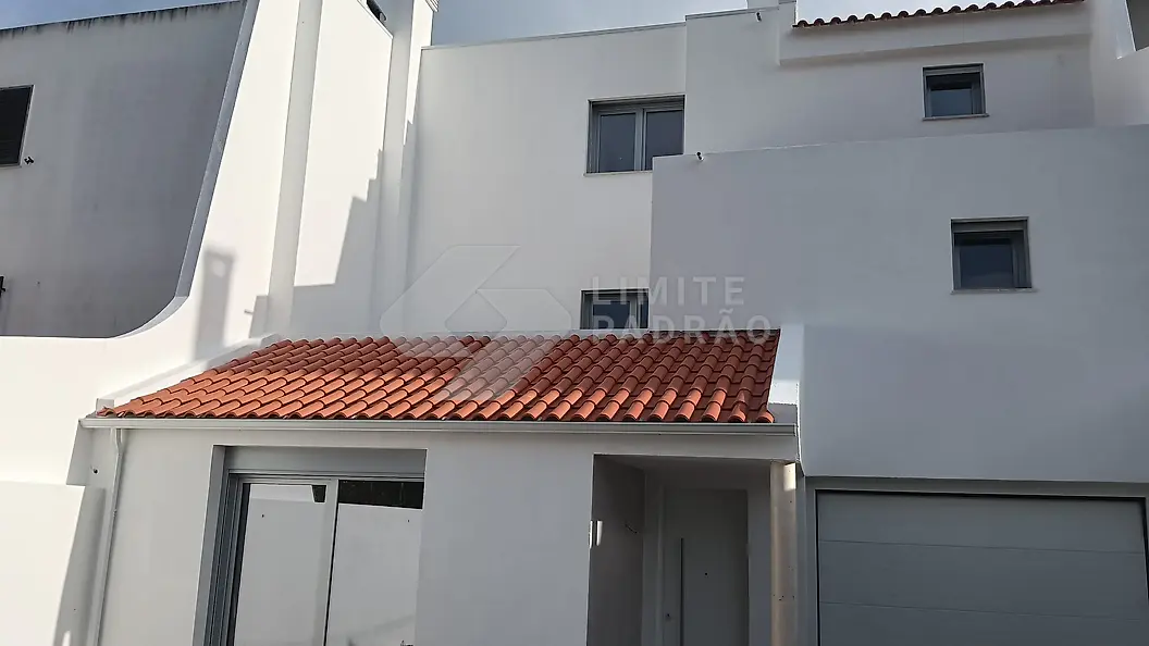 Moradia reabilitada: fachada branca, telhado em telha e portão de garagem novos