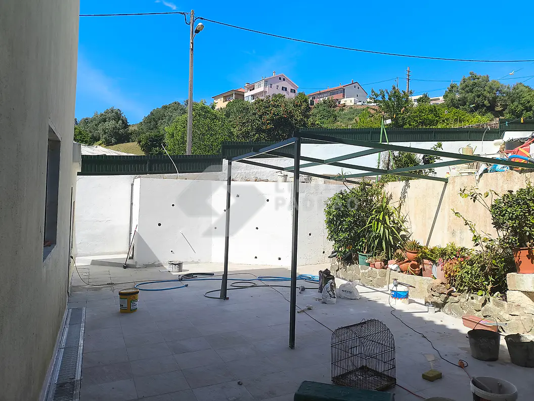 Em obra · pátio: estrutura metálica da pérgola montada; pavimento por aplicar