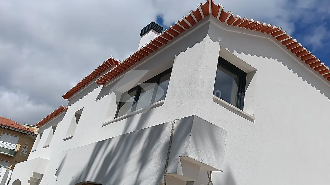 Construção de moradia: moradia branca com beirado em telha e caixilharia escura