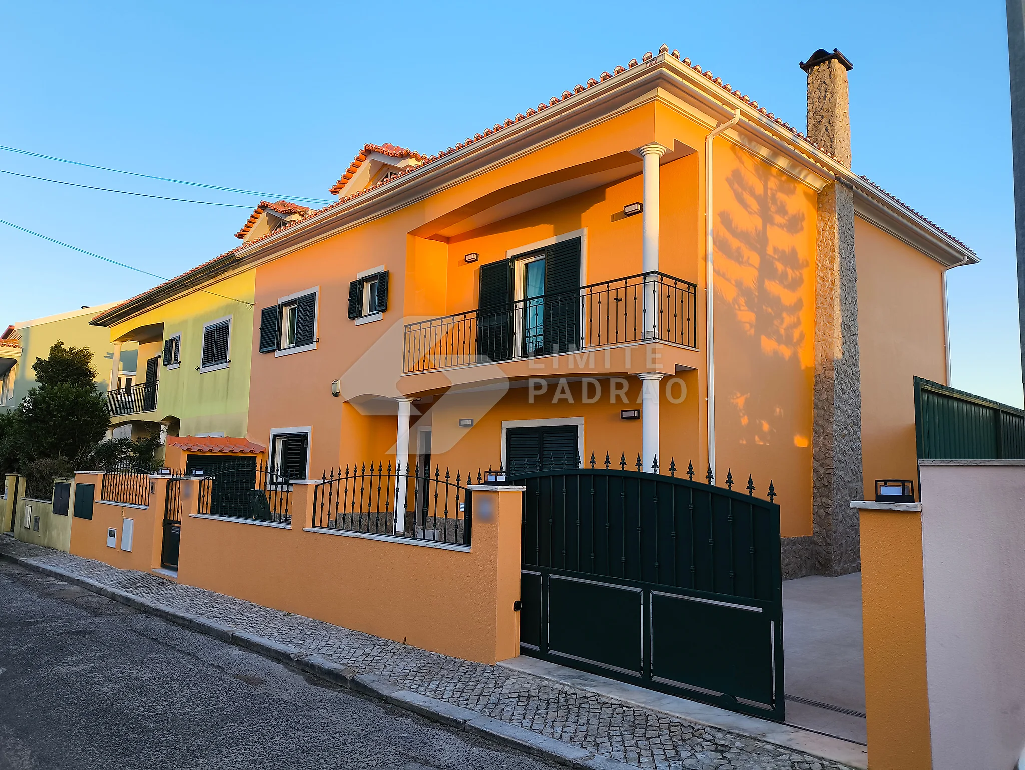 Remodelação de moradia: moradia de dois pisos com fachada laranja, muro e portão, ao fim da tarde